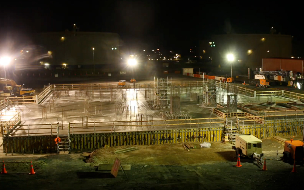 Nighttime concrete pour under floodlights at Marsden Point Oil Refinery, showing large foundation formwork and rebar installation by Advanced Concrete Pumping.