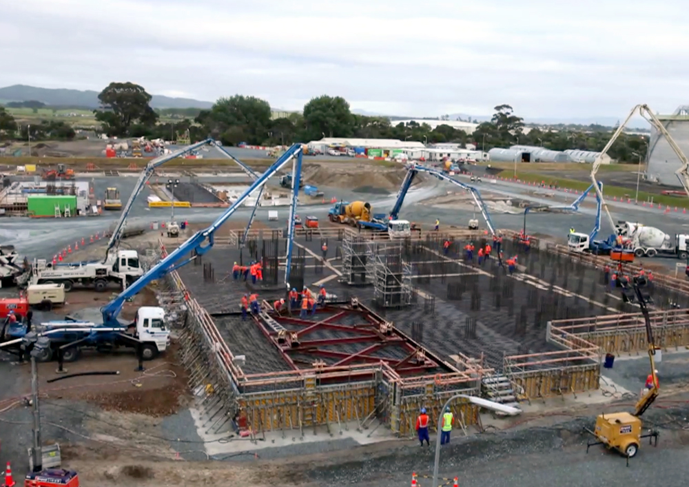 Large-scale concrete pour in progress at Marsden Point Oil Refinery, with multiple boom pumps and crew working on foundation slabs and reinforcement steel.