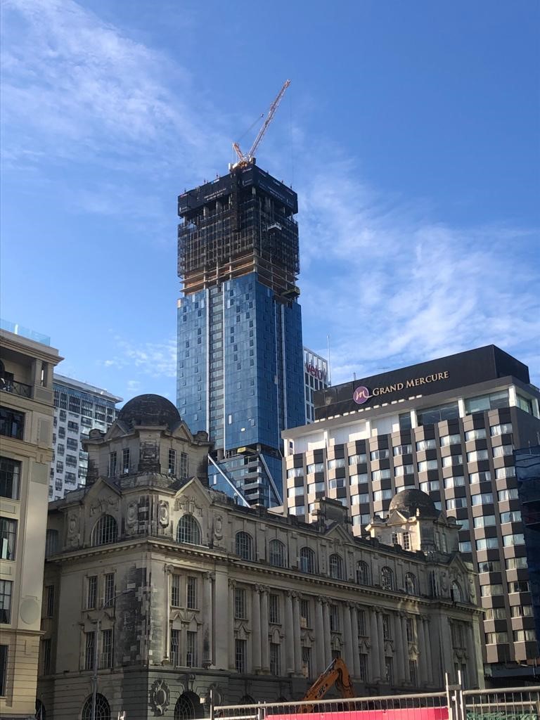 The Pacifica high-rise tower under construction in central Auckland, with cranes and upper levels being formed above the heritage Chief Post Office building.
