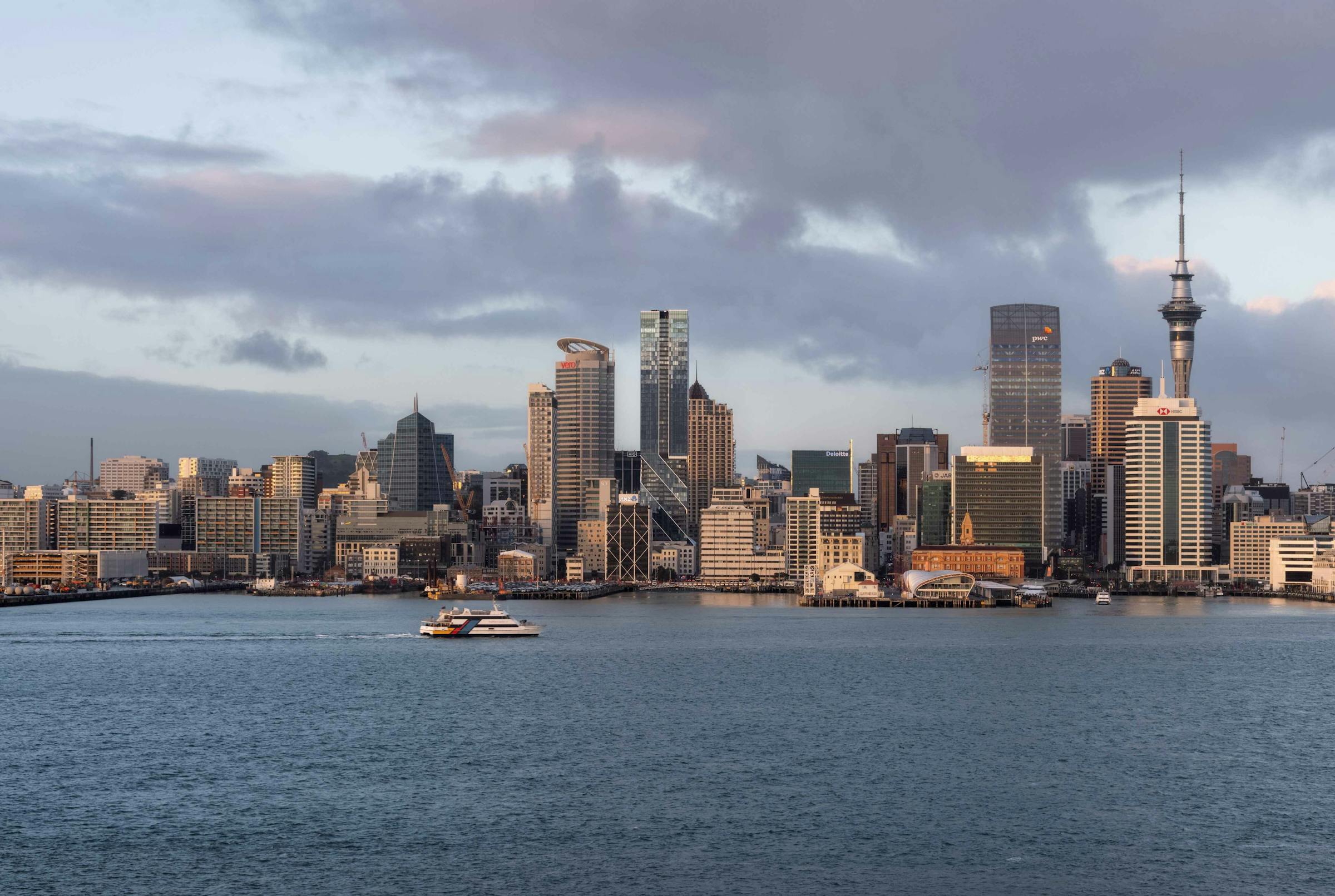 View of Auckland city skyline across the Waitematā Harbour, showing The Pacifica tower and Sky Tower among central business district buildings.
