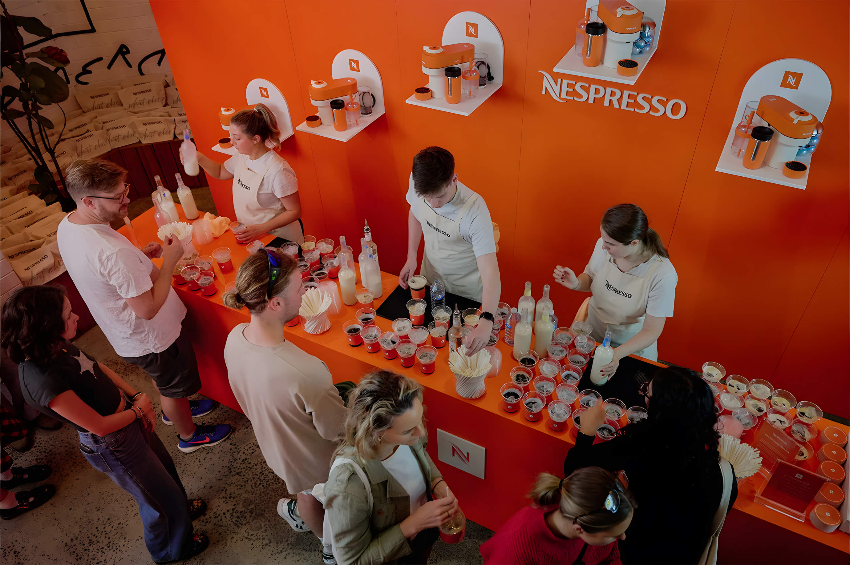 Guests queue at the Nespresso Happy Hour event bar in Bondi, where staff prepare coffee-based cocktails against a bright orange branded backdrop.