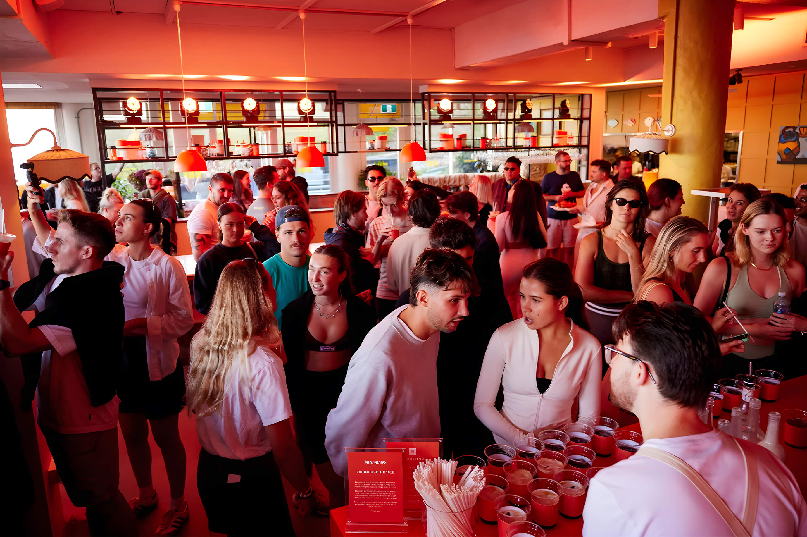 A packed crowd enjoys the Nespresso Happy Hour event at Bondi, with red lighting and drinks creating a lively atmosphere.