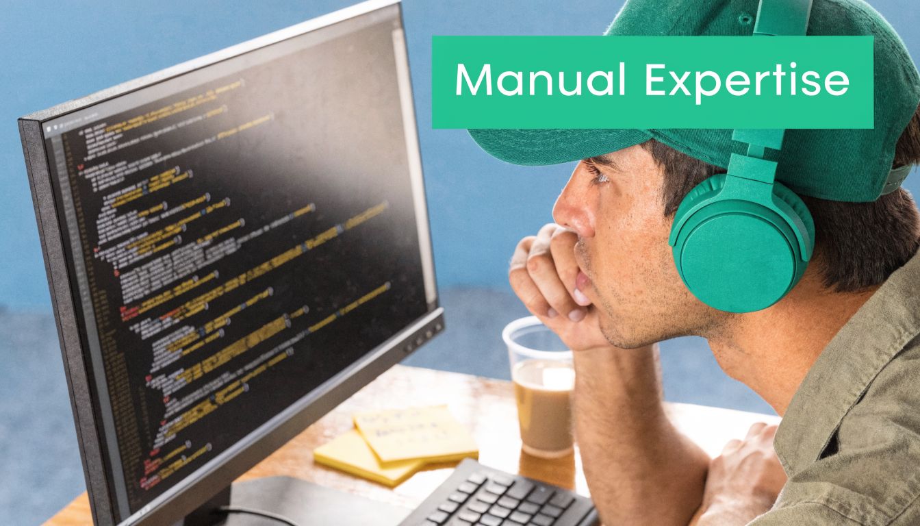 A male software developer in a cap and headphones studying code on a desktop computer screen.