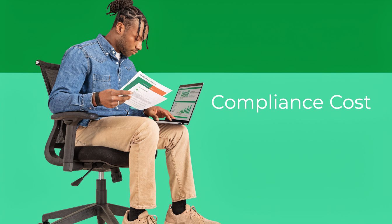 A professional man sitting on an office chair holding financial documents while working on a laptop computer.