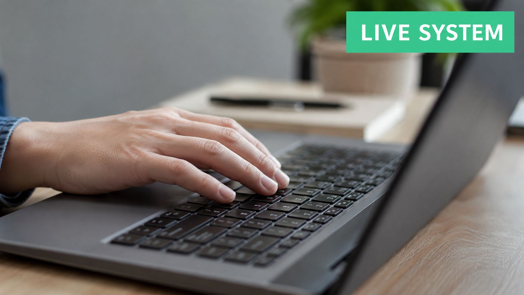 A close-up view of a person typing on a laptop keyboard at a wooden desk.