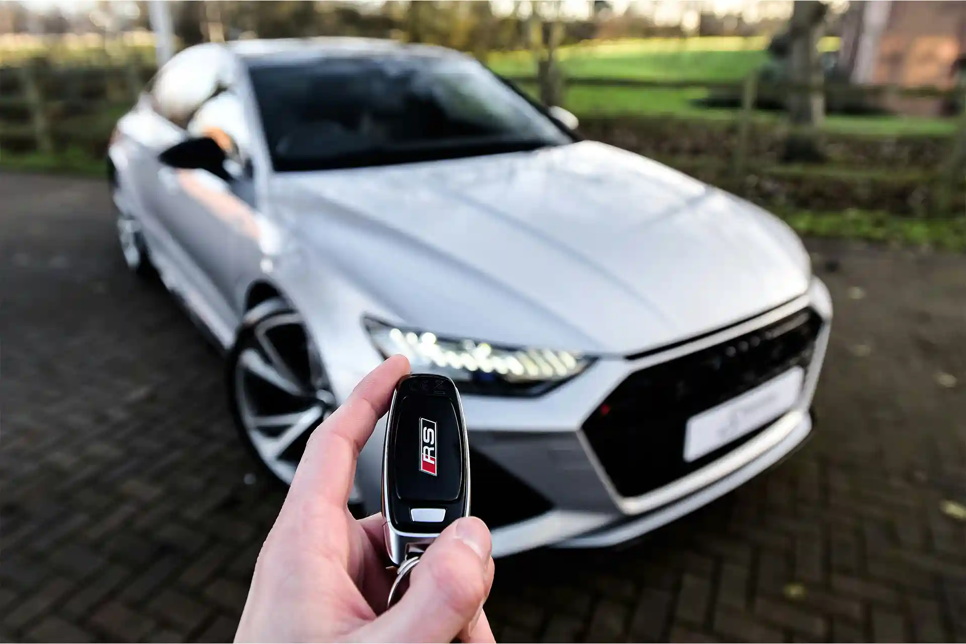 A man holds car keys in the air in front of a new silver used car