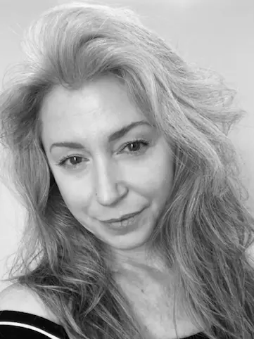 Black and white portrait of a woman with long wavy hair and a slight smile, wearing an off-shoulder top.