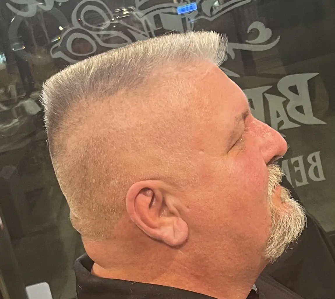 Side profile of a man with a crew cut hairstyle and a trimmed mustache and goatee.