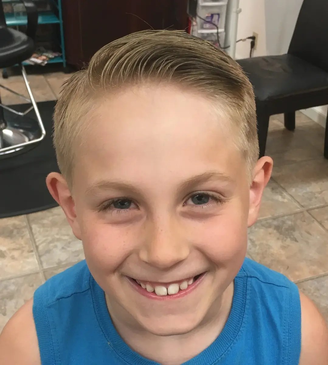 Smiling young boy with short, neatly combed blond hair wearing a blue sleeveless shirt.