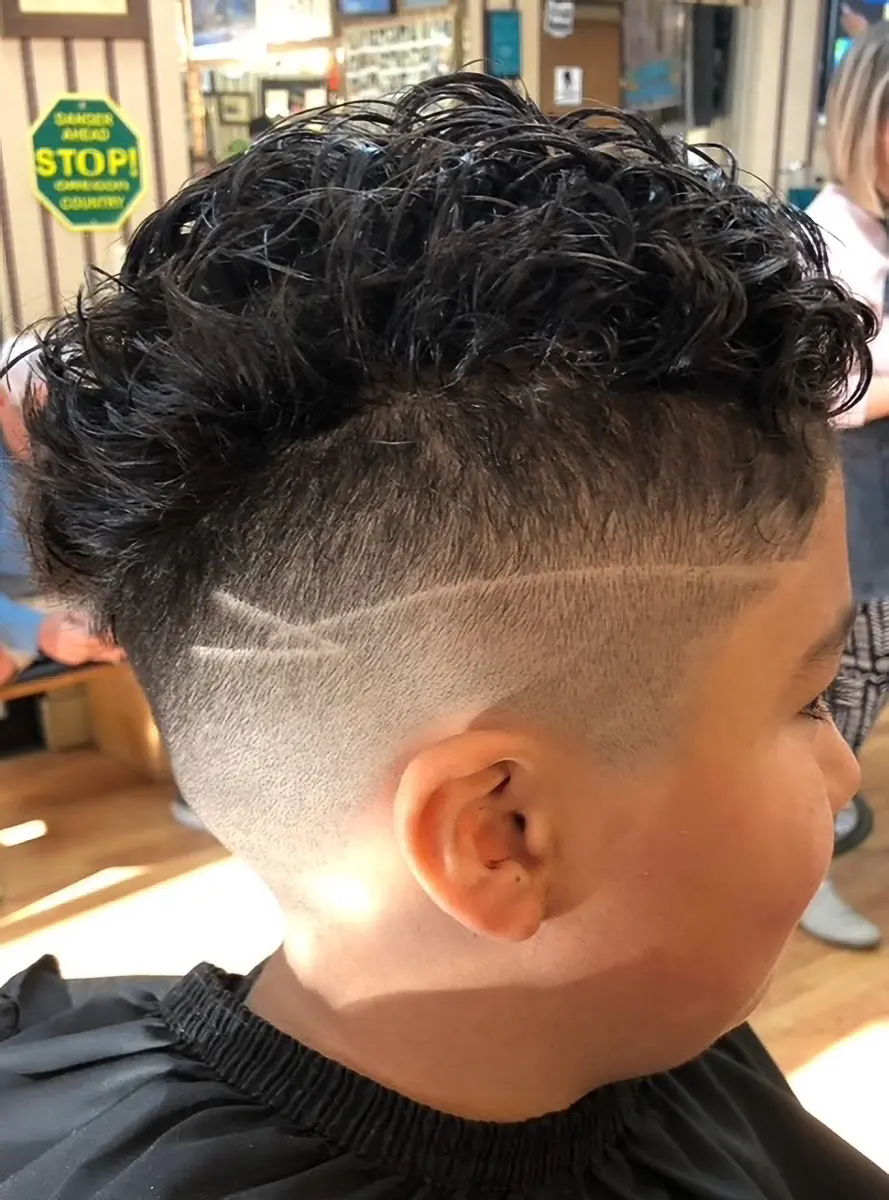 Side view of a person with a curly top haircut featuring a faded undercut and two shaved lines on the side.