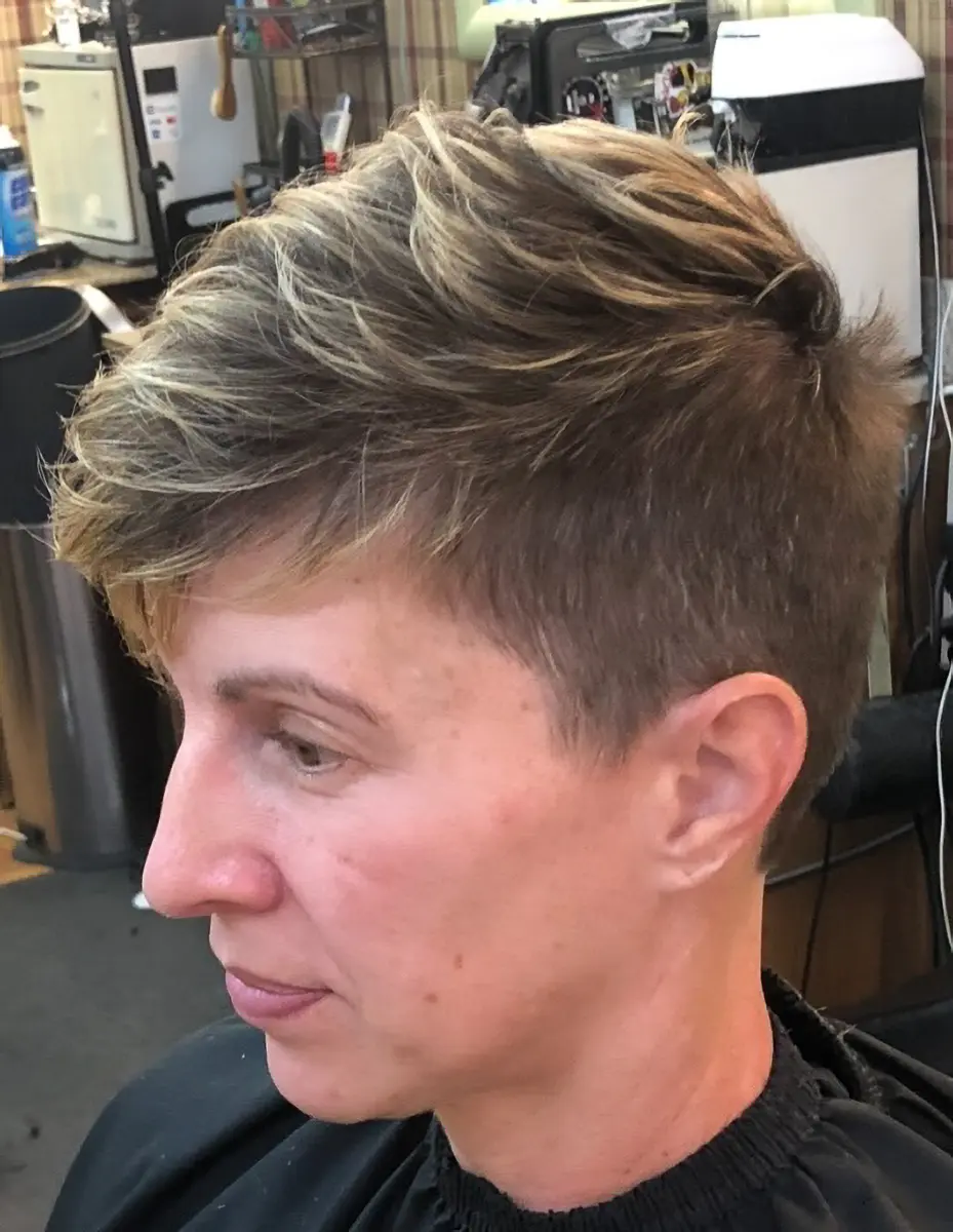 Side profile of a person with short, textured hair styled with blonde highlights in a barbershop setting.