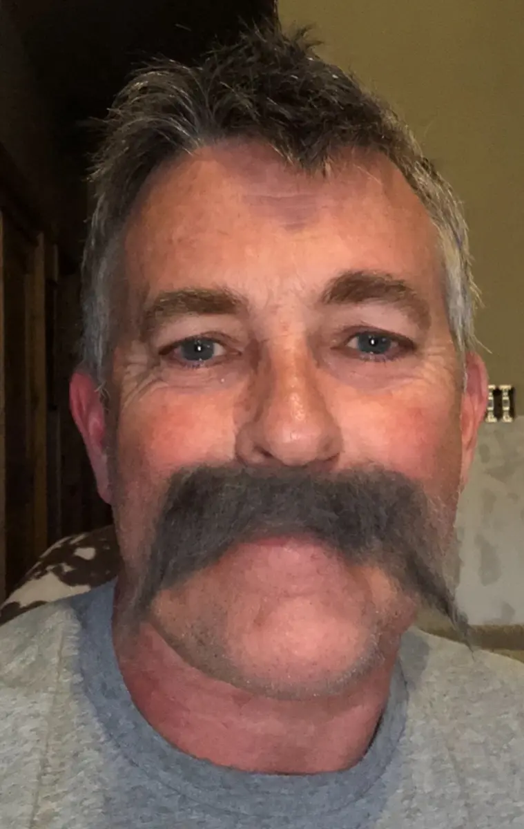 Middle-aged man with blue eyes and large, bushy dark mustache wearing a gray shirt.