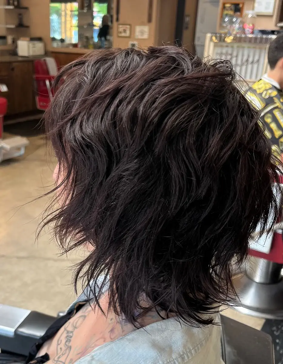 Side view of a person with layered, wavy dark brown hair in a salon setting.