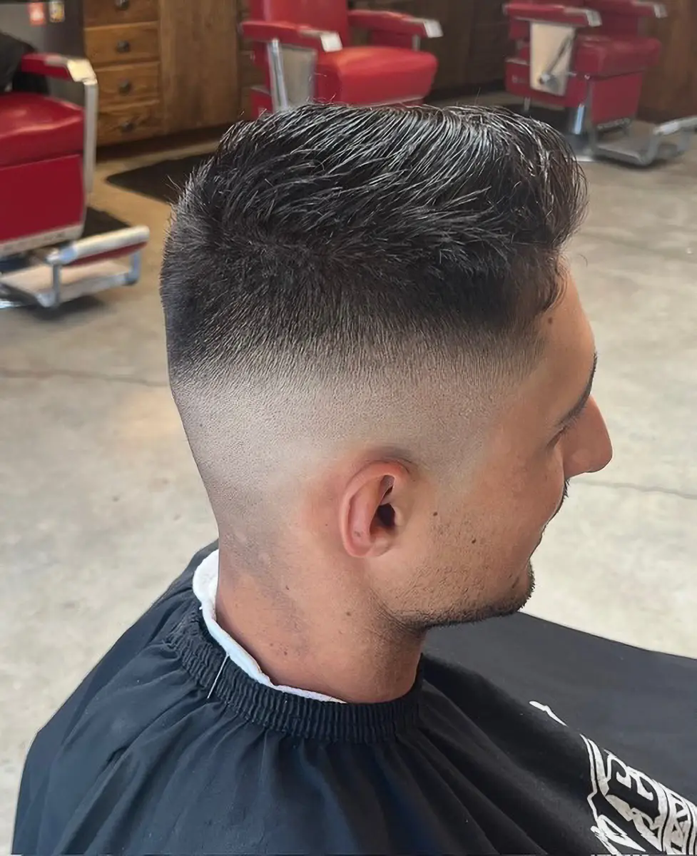 Side view of a man with a clean fade haircut and textured top sitting in a barbershop chair.