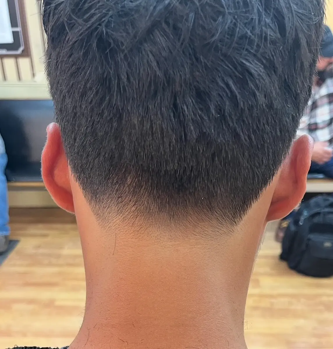 Back of a person's head showing a fresh tapered haircut with short black hair and clean neckline.