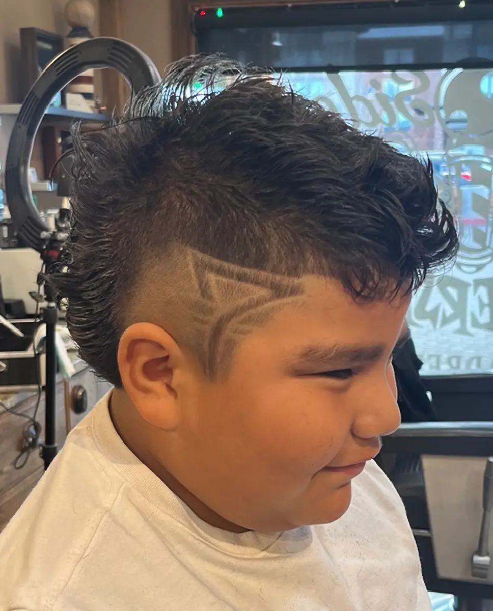 Side profile of a boy with a mohawk haircut featuring shaved geometric patterns on the side.