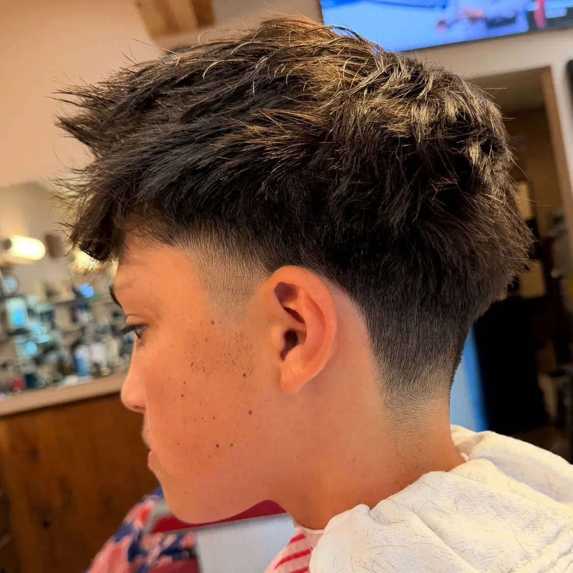 Side profile of a person with a fresh textured haircut featuring a low fade around the ears and neck.