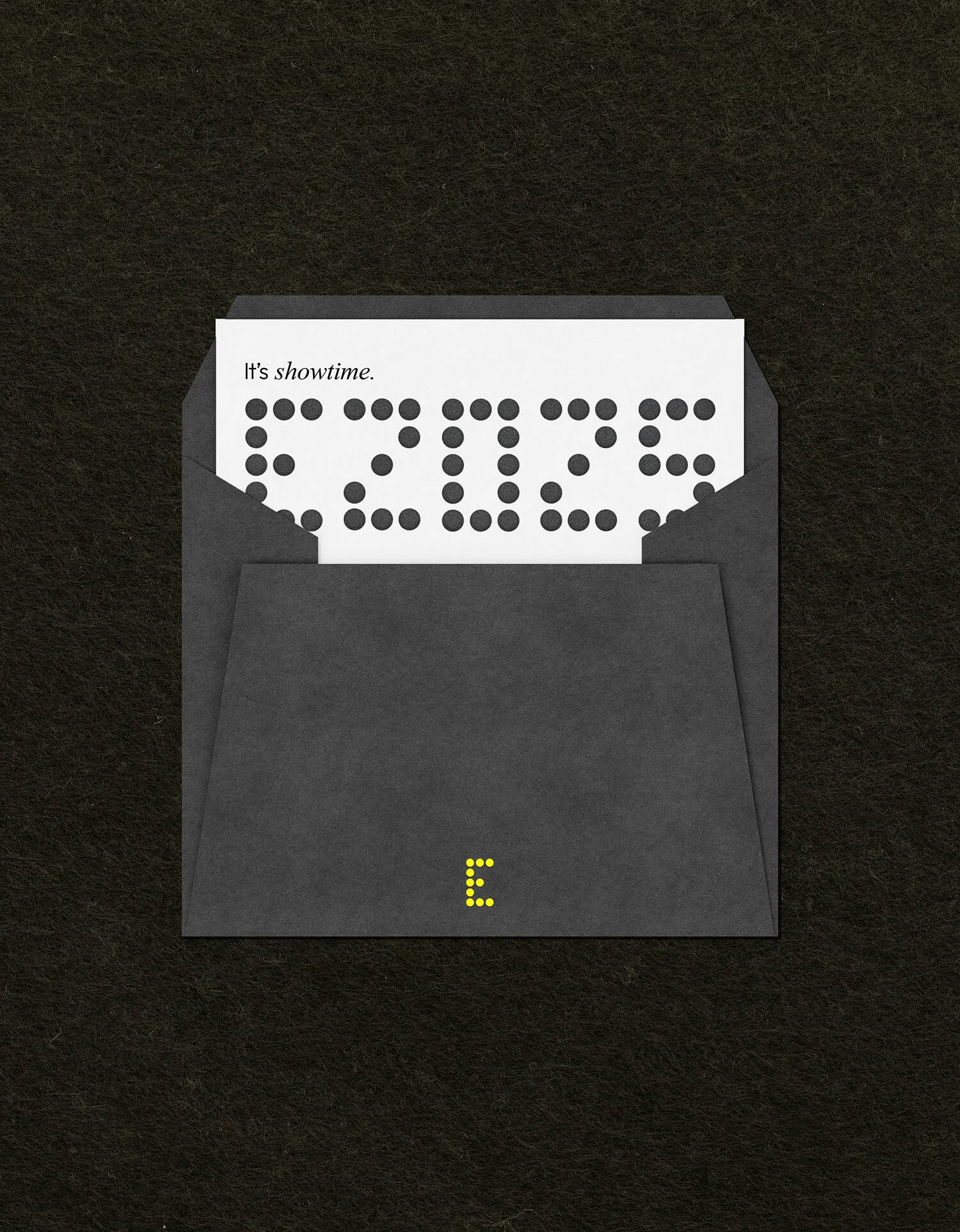 Black envelope with white card inside that says 'It's showtime.' above the word 'E2025' spelled out in black dots.