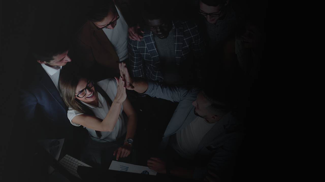 Group of diverse coworkers giving a high-five in an office setting with documents and keyboard visible.
