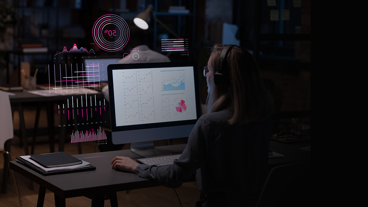 Person wearing headphones working on a computer displaying various charts and graphs with digital data overlays in an office.