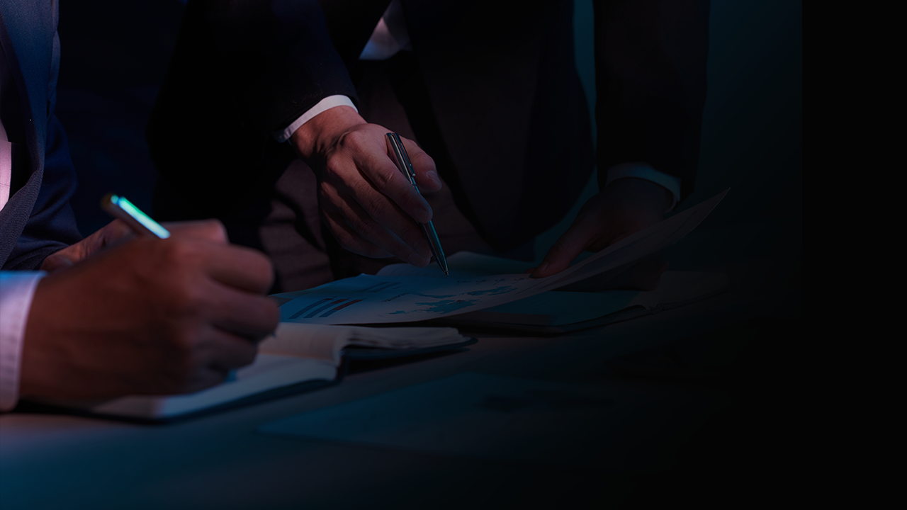 Two people in business suits working with documents and taking notes in low light.