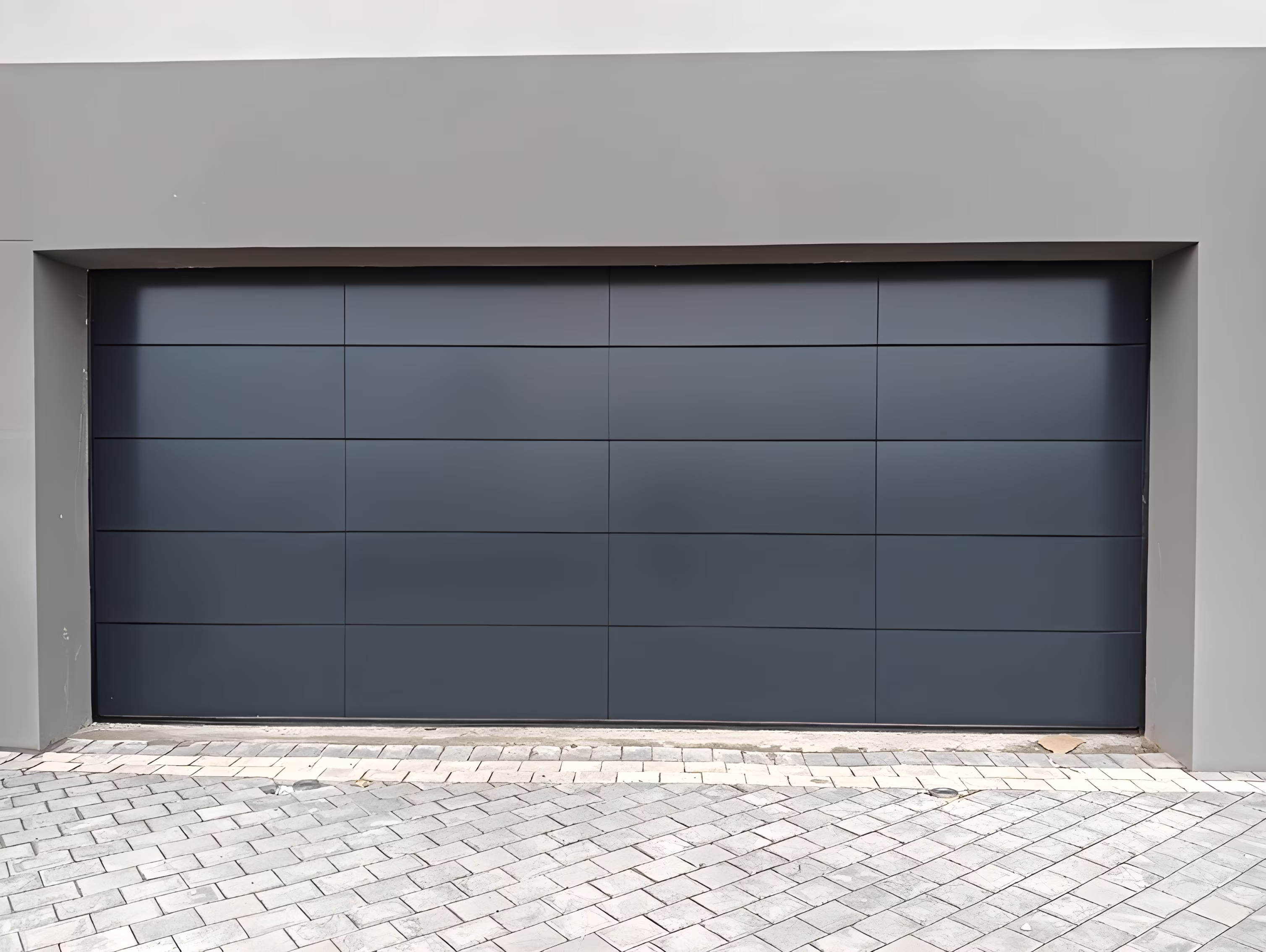 Modern dark gray sectional ACM garage door with horizontal panel design set in a light gray frame and paved driveway.