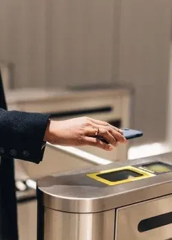 Personne utilisant un smartphone pour accéder à un tourniquet avec lecteur sans contact.