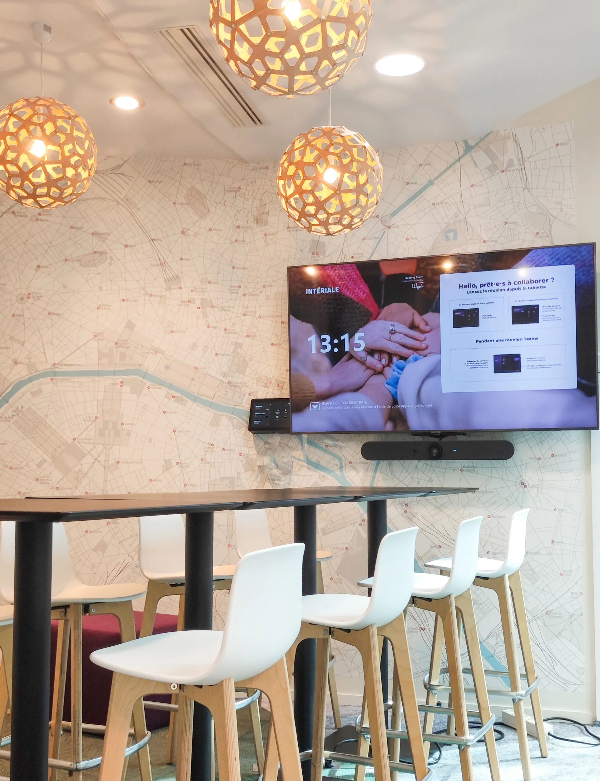 Salle de réunion avec table haute entourée de chaises blanches et un grand écran affichant une invitation à collaborer en visioconférence.