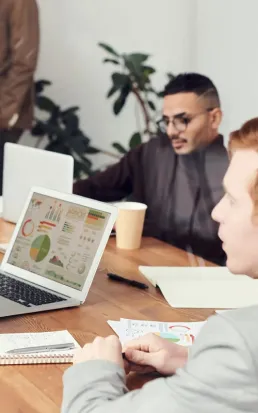 Deux professionnels discutant de graphiques et de données sur des ordinateurs portables lors d'une réunion.