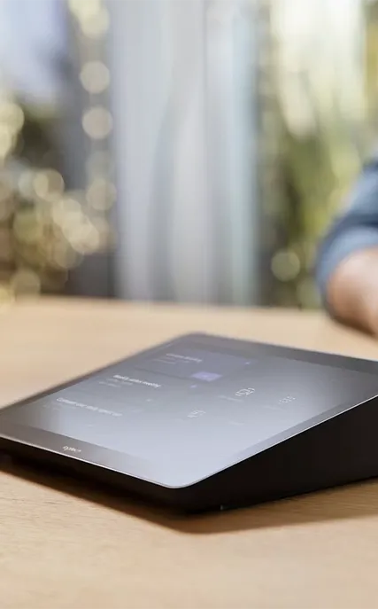 Appareil de conférence noir posé sur une table en bois avec un écran tactile affichant des options de réunion.
