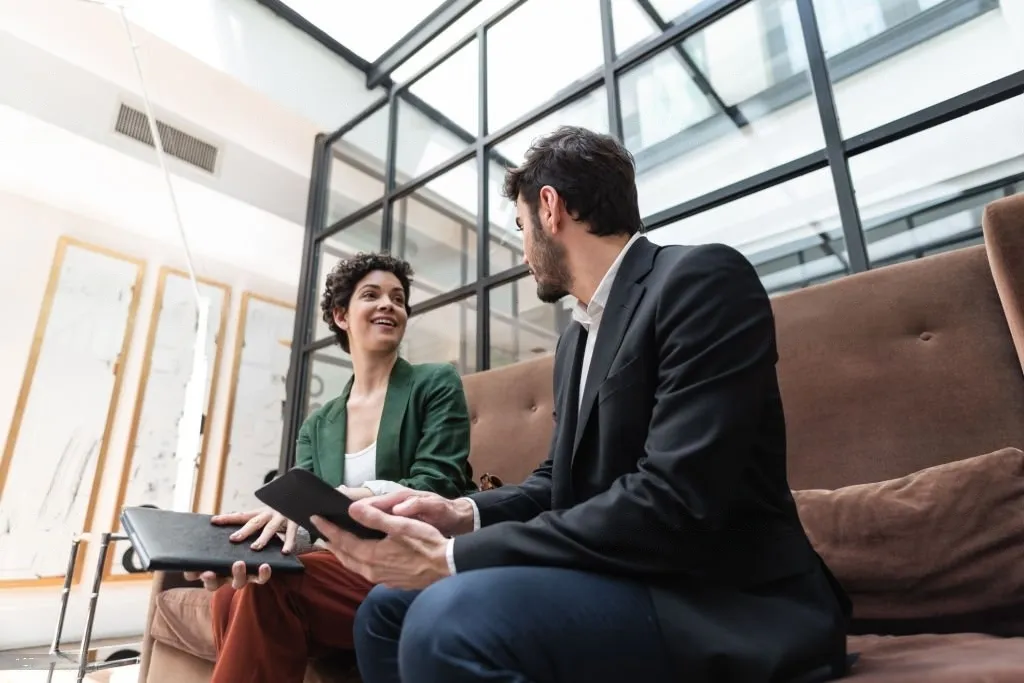 Deux professionnels souriants discutant dans un bureau moderne avec des tablettes numériques en main.