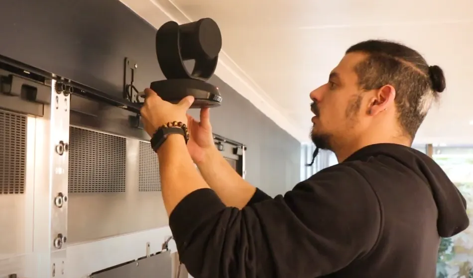 Un homme installe une caméra PTZ noire sur un support mural.