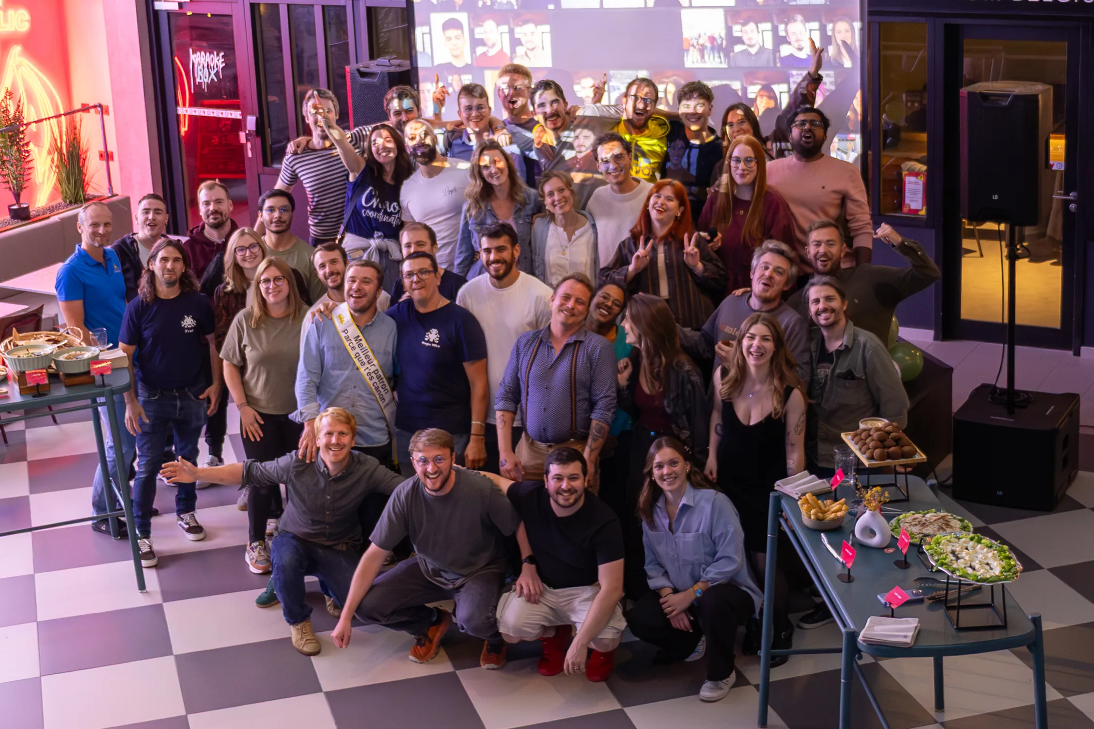 Groupe de personnes souriantes posant pour une photo lors d'un événement avec nourriture sur des tables.
