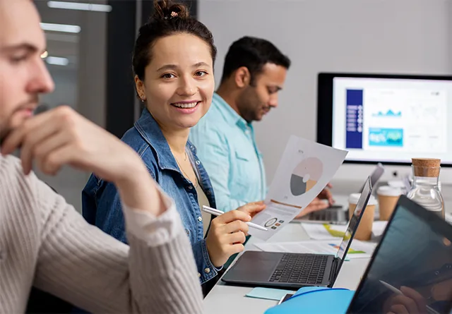 Woman smiling while holding an SEO analytics chart in a team meeting.