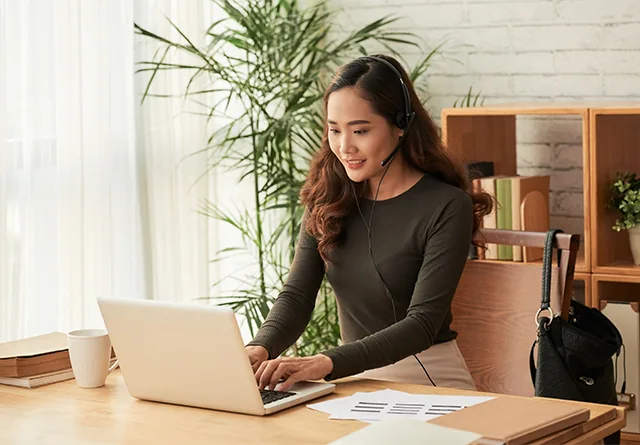 Woman wearing a headset typing on a laptop, comparing freelance hiring platforms.