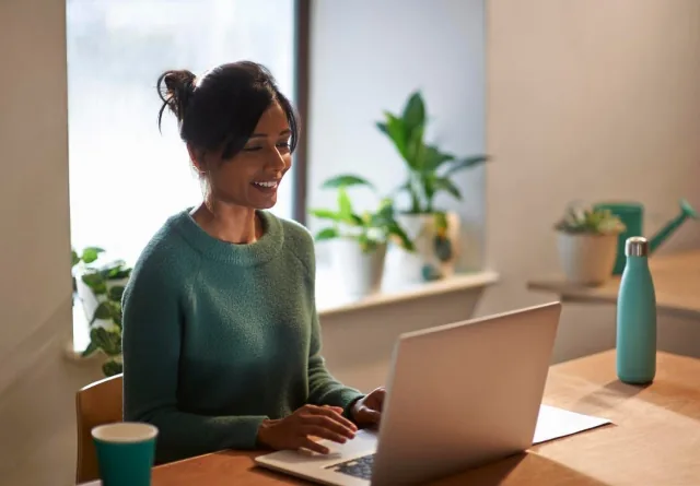 Woman smiling while managing PPC campaigns on her laptop at home.