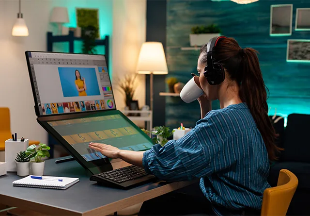 Graphic designer editing a photo on dual monitors while sipping coffee.