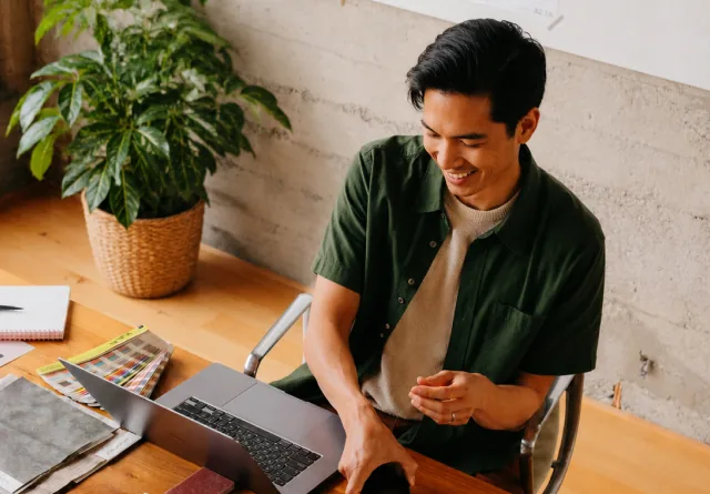 Man smiling at his laptop while reviewing Facebook advertising costs.