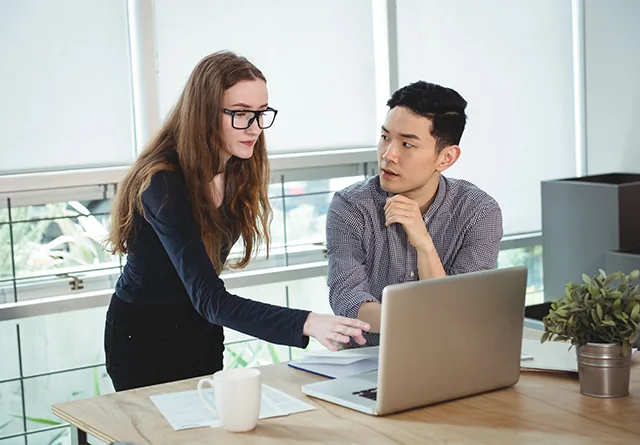 Colleague pointing at a laptop while discussing in-house vs. outsourced marketing.