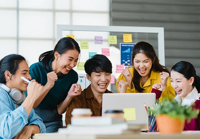 Marketing team cheering together while reviewing results on a laptop.