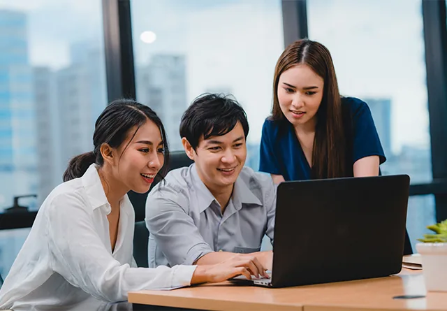 Three colleagues reviewing a laptop while discussing outsourcing vs. offshoring.