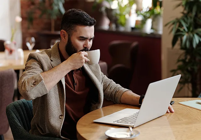 Man sipping coffee while comparing Upwork vs. Toptal vs. GrowthAssistant.