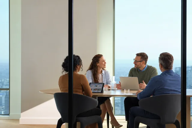 Four colleagues meeting around a table in a glass-walled conference room