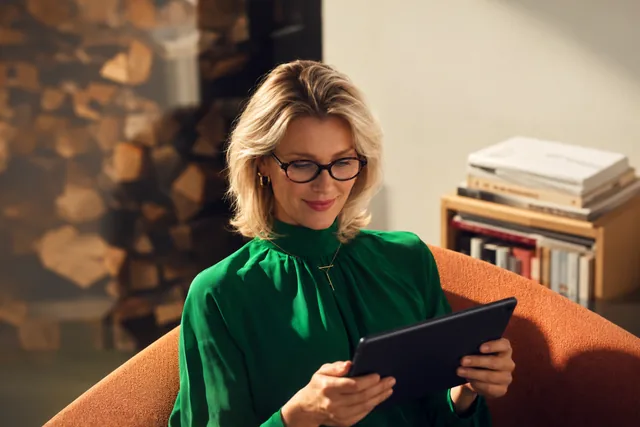 Woman in a green blouse reading on a tablet in a bright room
