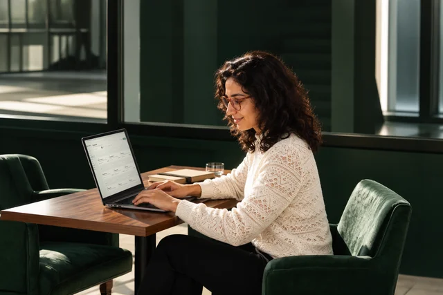 Woman working on a laptop at a wooden table in a green cafe