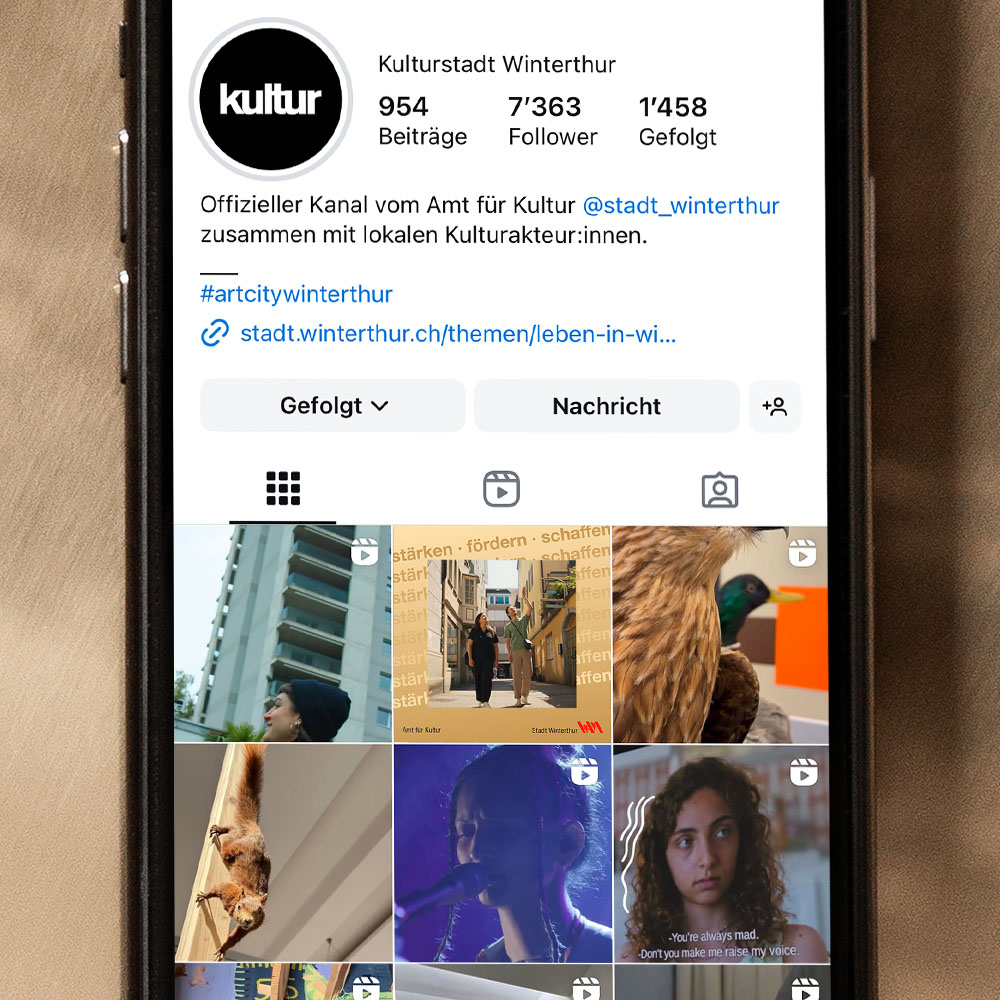 Ein Handy liegt auf goldigem Untergrund. Auf dem Bildschirm ist das Instagramprofil des Amts für Kultur zu sehen. 
