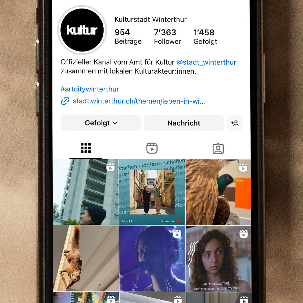 Ein Handy liegt auf goldigem Untergrund. Auf dem Bildschirm ist das Instagramprofil des Amts für Kultur zu sehen. 