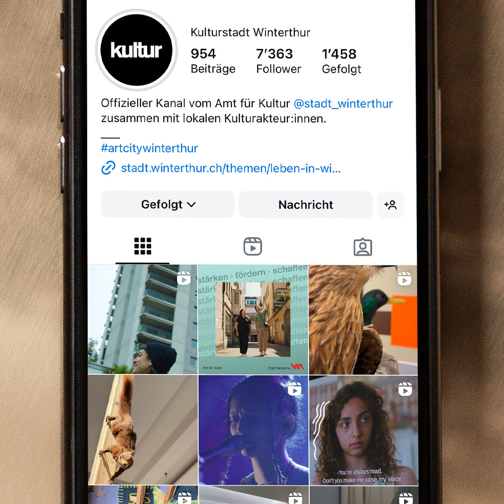 Ein Handy liegt auf goldigem Untergrund. Auf dem Bildschirm ist das Instagramprofil des Amts für Kultur zu sehen. 