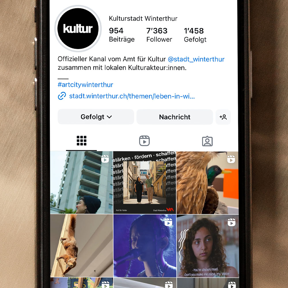 Ein Handy liegt auf goldigem Untergrund. Auf dem Bildschirm ist das Instagramprofil des Amts für Kultur zu sehen. 