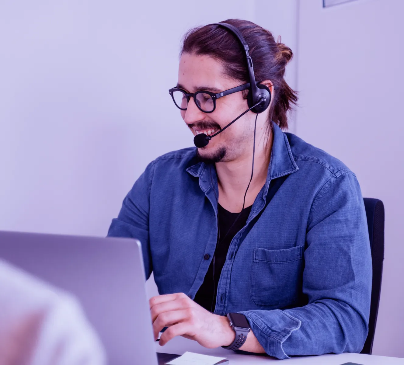 Man wearing a headset sitting smiling looking at the laptop.